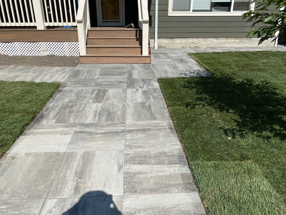 Stone pathway leading from a deck to the backyard flanked by green grass and a residential home