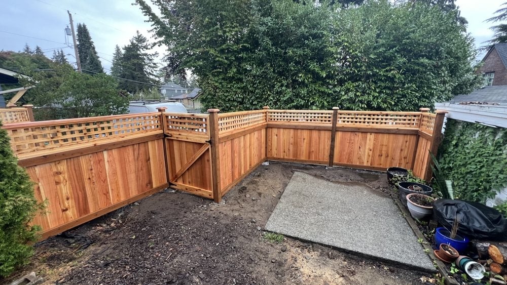 New wooden fence and gate enclosing a residential backyard with pea gravel ground and landscaping