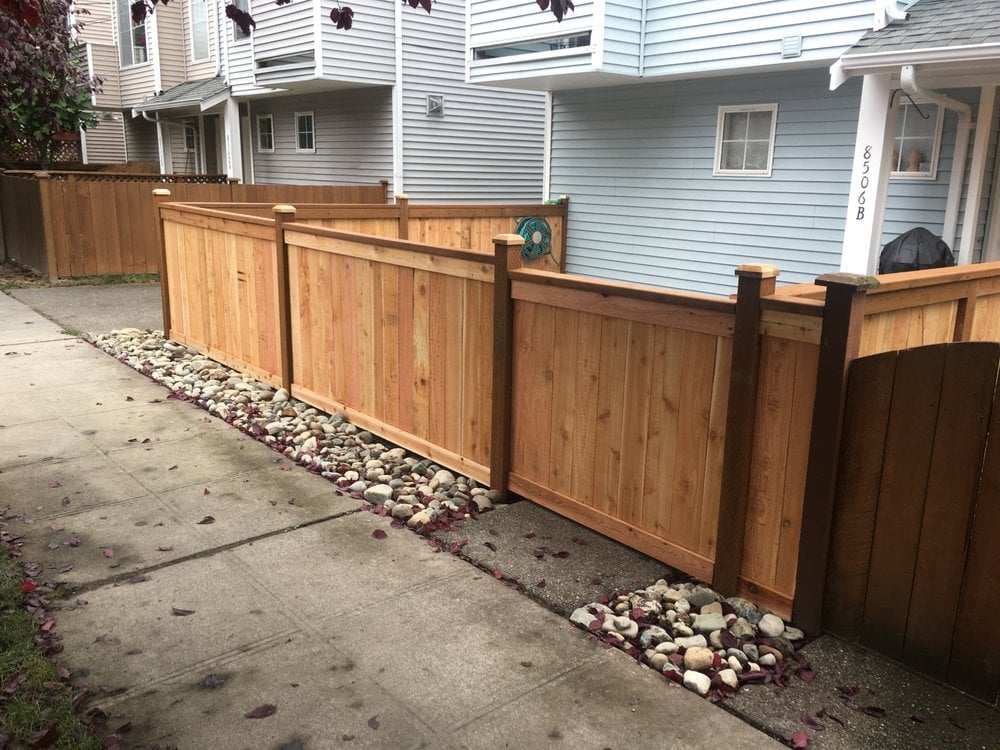 Wooden fence with gate along a residential driveway with white houses in the background