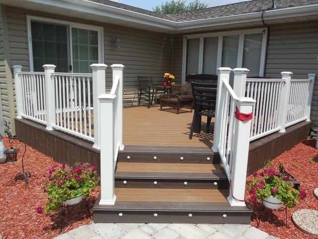 Front deck with white railings, brown composite steps, and red mulch landscaping on a residential home