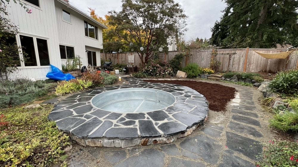 Circular stone patio with geometric pattern in a backyard surrounded by landscaping and trees