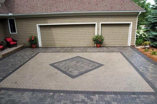 Two-car garage with tan brick facade and geometric patterned driveway with diamond inlay in contrasting pavers