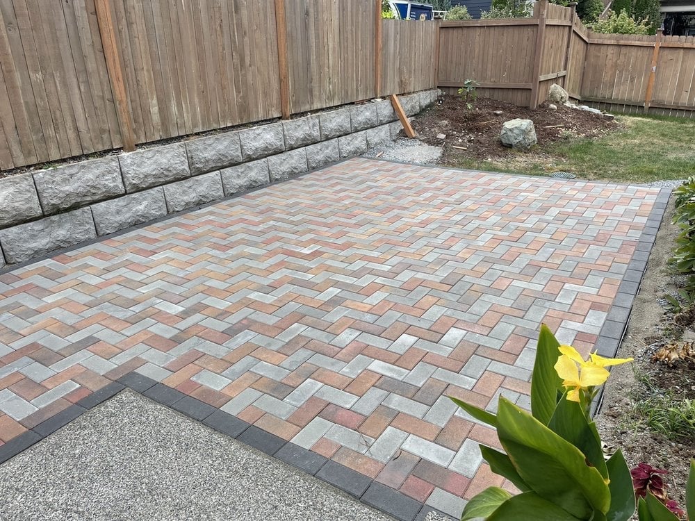 New brick patio with herringbone pattern, concrete retaining wall, and wooden fence in a backyard landscaping project