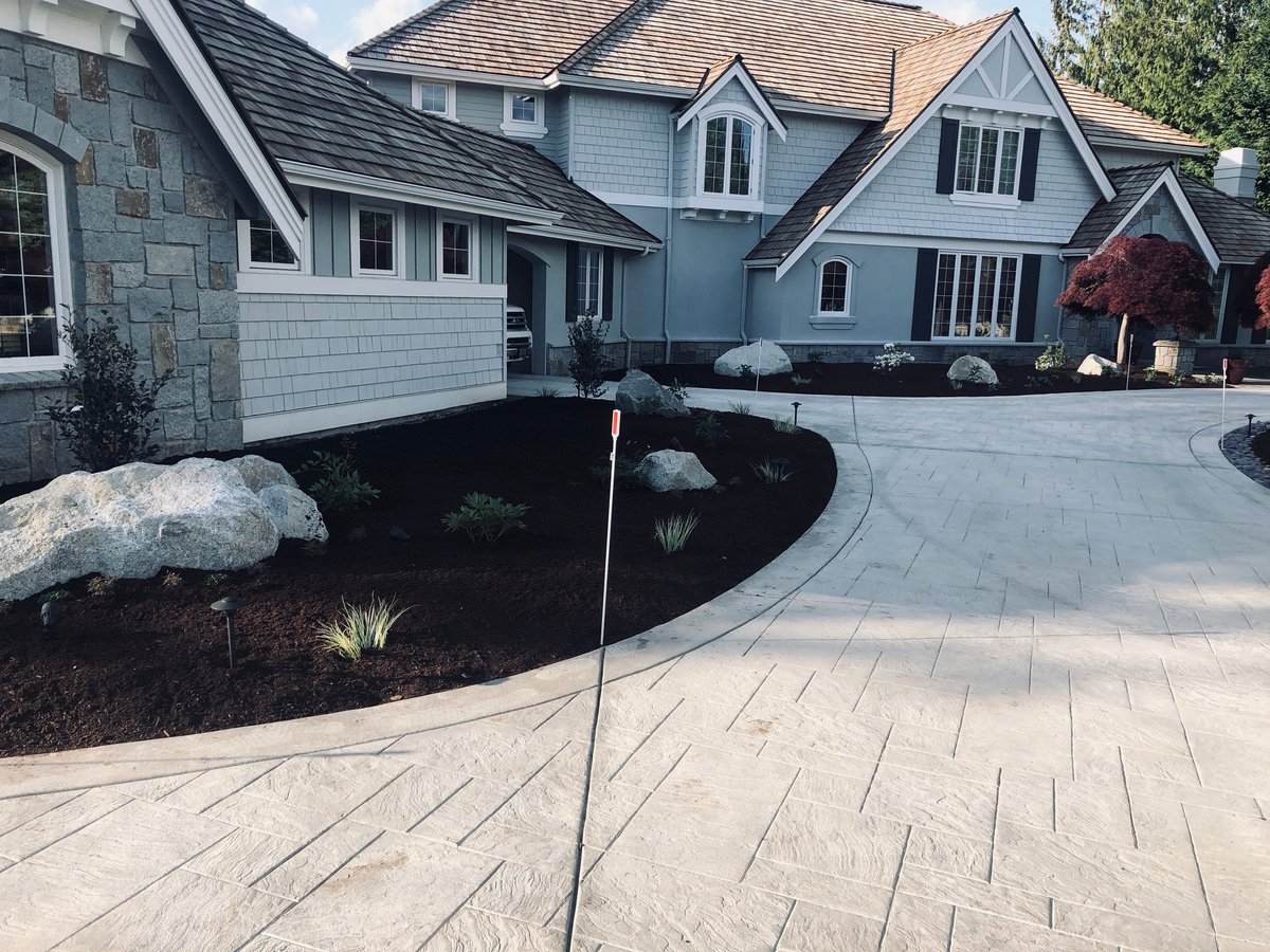 Modern two-story home with fresh gray-blue and white exterior paint, large paver driveway, and circular mulch landscaping bed in the front