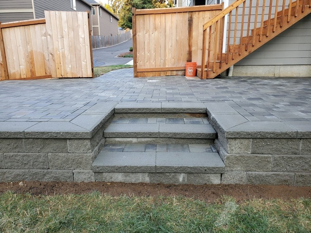 Stone steps descending from a paved patio, with wooden fencing and a house visible in the background