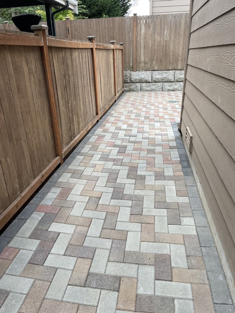 Narrow side yard with a herringbone-patterned paver walkway bordered by wooden fences and house siding