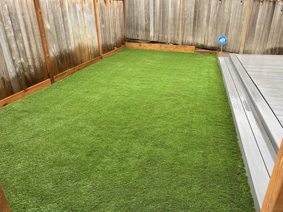 Backyard with bright green artificial turf, wooden fence, and gray composite deck on the right side