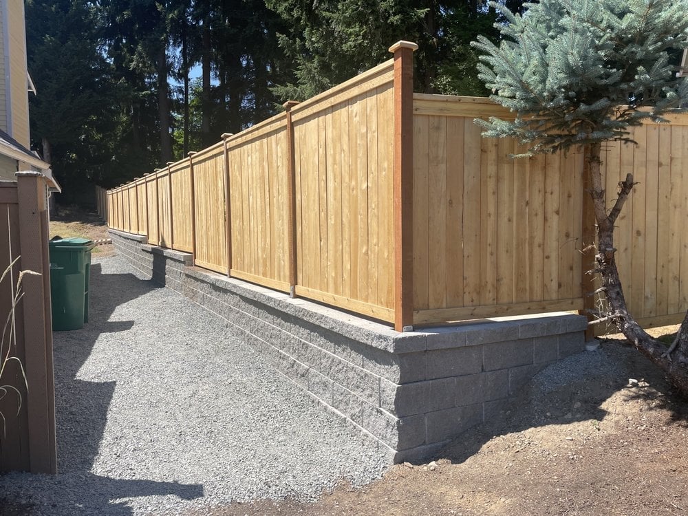 Newly constructed wooden privacy fence with concrete foundation blocks along a gravel pathway