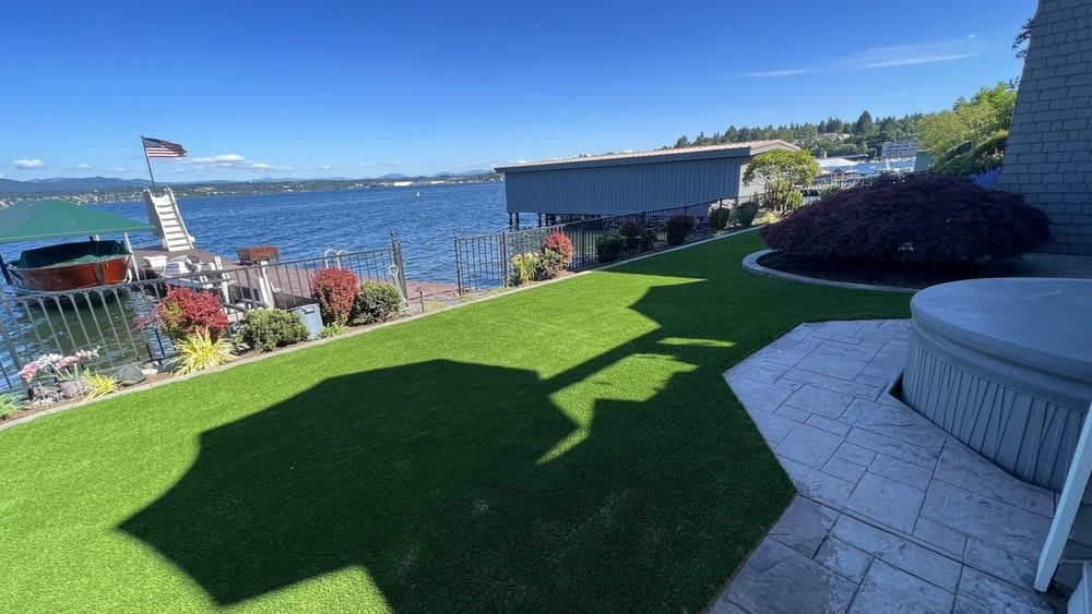 Waterfront backyard with artificial green lawn, patio, and bay view under clear blue sky