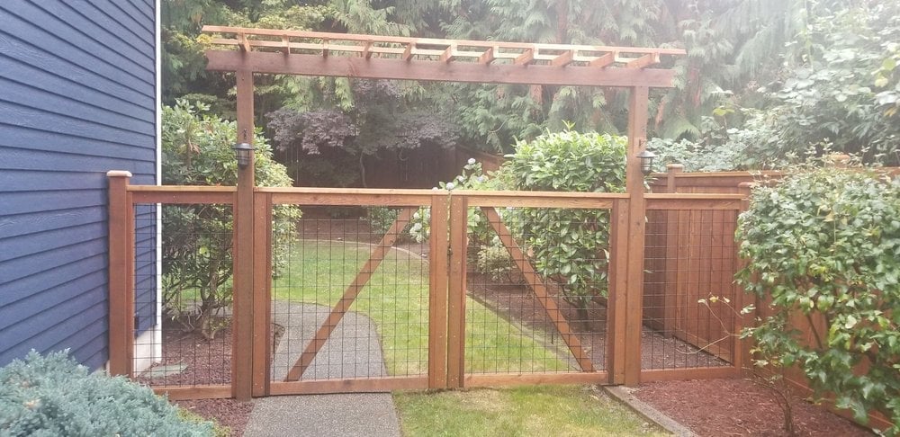 Wooden garden gate and fence enclosure with wire mesh panels in a backyard setting surrounded by greenery